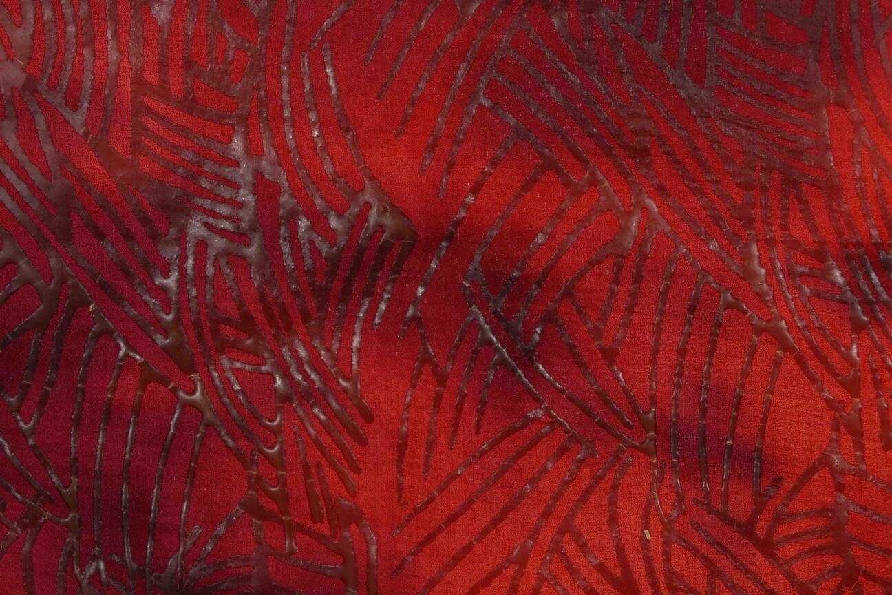 Fabric in red nuances with a wax design. The second step in coloring a fabric with the batik process is stamping the red fabric with hot wax in a design motif